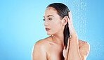 Shower, water and face of woman on blue background for grooming, cleaning and body wellness in studio. Skincare, bathroom mockup and serious girl model washing hair for hygiene, hydration and beauty