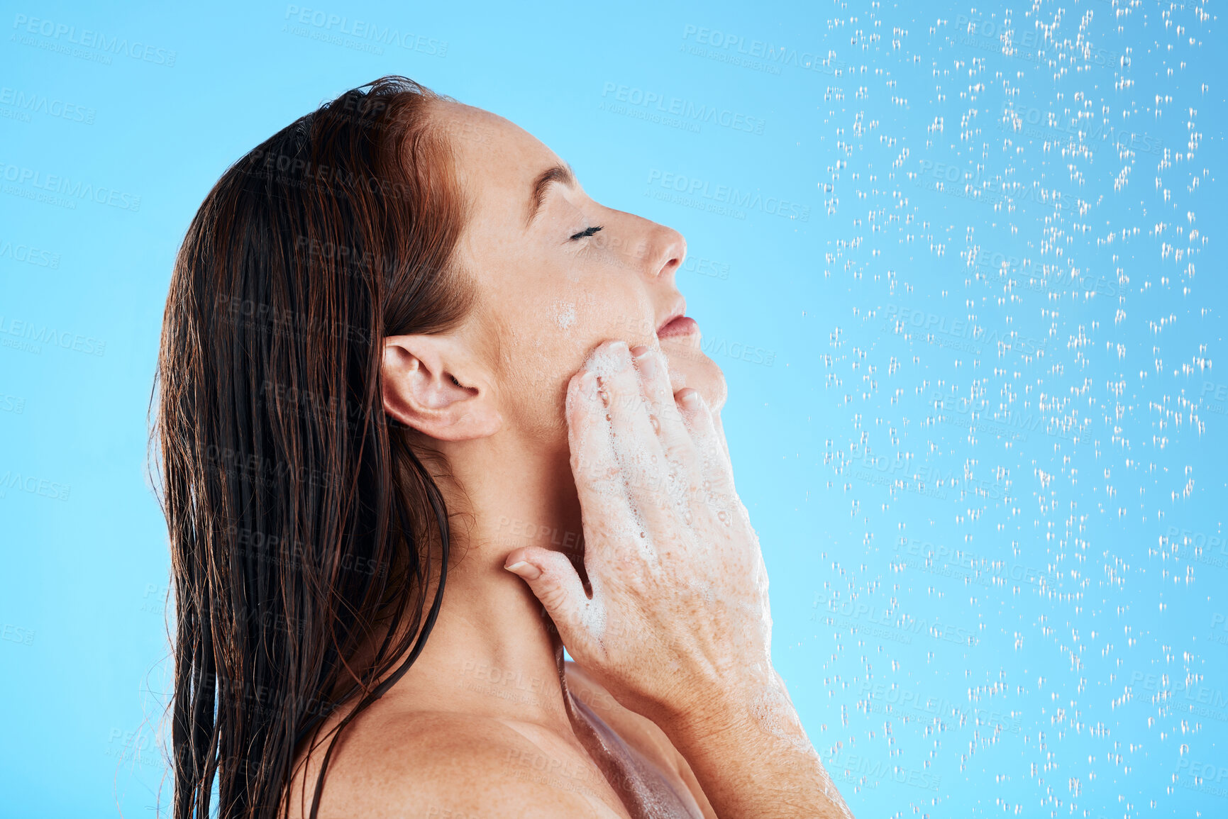 Buy stock photo Shower, water and woman soap on face in studio, blue background and hygiene cleaning. Relax female model washing facial with wet drops, foam and beauty of skincare cosmetics, self care and backdrop