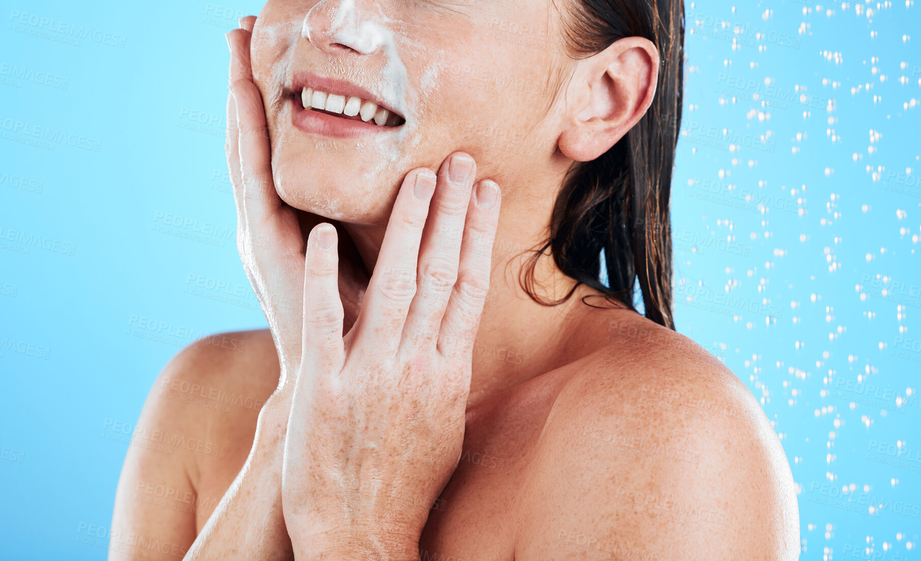 Buy stock photo Woman face, wash and shower studio with a young female hands doing skincare and beauty routine. Bathroom, dermatology and facial treatment of a model smile from cleaning and isolated blue background