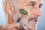 Elderly man, jade roller and face for skincare with smile, self care and wellness in studio by white background. Elderly model, facial massage and beauty with stone product, cosmetic and dermatology