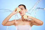 Beauty, skincare and water splash with woman and lemon in studio for natural cosmetics, nutrition and detox. Glow, fruits and hydration with female on blue background for diet, face and vitamin c