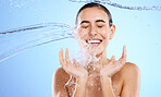 Water splash, smile and woman cleaning in studio, blue background and beauty of sustainable skincare. Happy female model, wet and shower for hygiene, facial hydration and aqua bath on color backdrop 