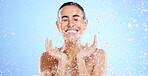 Water splash, face and woman shower in studio, blue background and healthy beauty of wellness skincare. Happy female model, wet drops and cleaning of facial, aqua hydration or smile on color backdrop