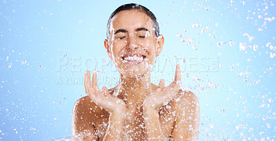 Buy stock photo Water splash, face and woman shower in studio, blue background and healthy beauty of wellness skincare. Happy female model, wet drops and cleaning of facial, aqua hydration or smile on color backdrop