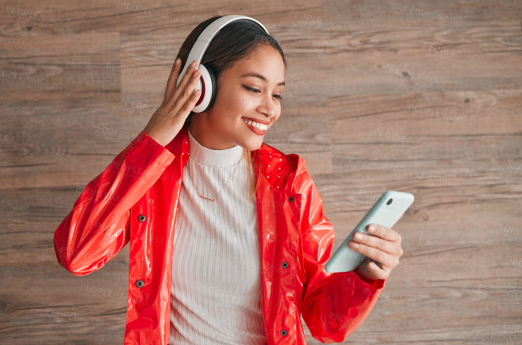 Buy stock photo Phone, headphones and happy woman with music isolated on wood background, audio streaming and mobile app. Gen z student or biracial person listening on cellphone, electronics sound and technology
