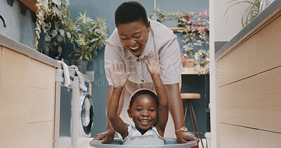 Playful black mother pushing her daughter around in a laundry basket at home. Young woman and her child playing and having fun while spending time at home