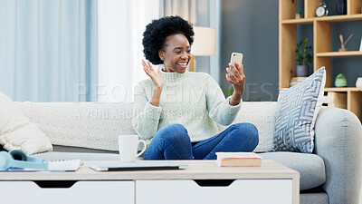 Happy African woman talking on the phone and waving hello while on a video call with friends at home. Cheerful black female with afro laughing while having a funny conversation on a mobile app