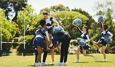 Cheerleaders doing routine with pom poms on football field, Stock