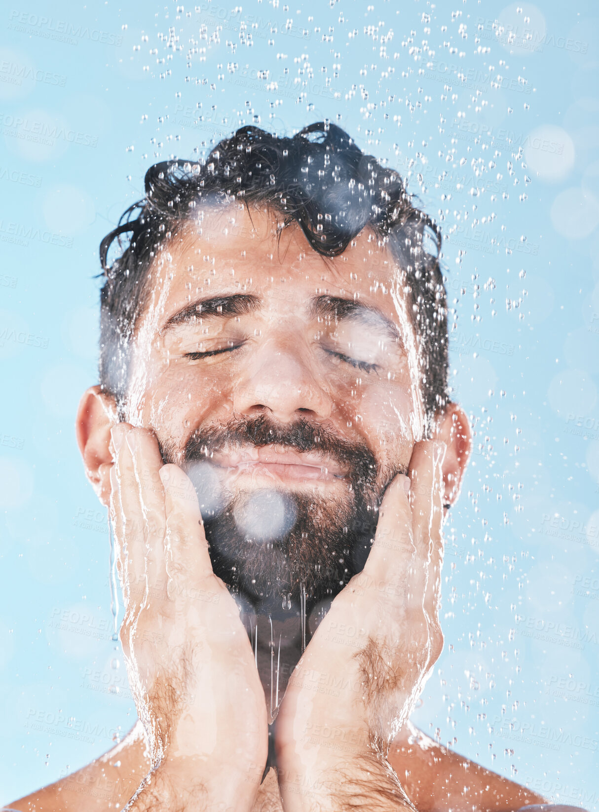 Buy stock photo Face, skincare shower and water splash of man in studio isolated on a blue background. Water drops, dermatology and male model washing, cleaning or bathing for healthy skin, wellness and hygiene.