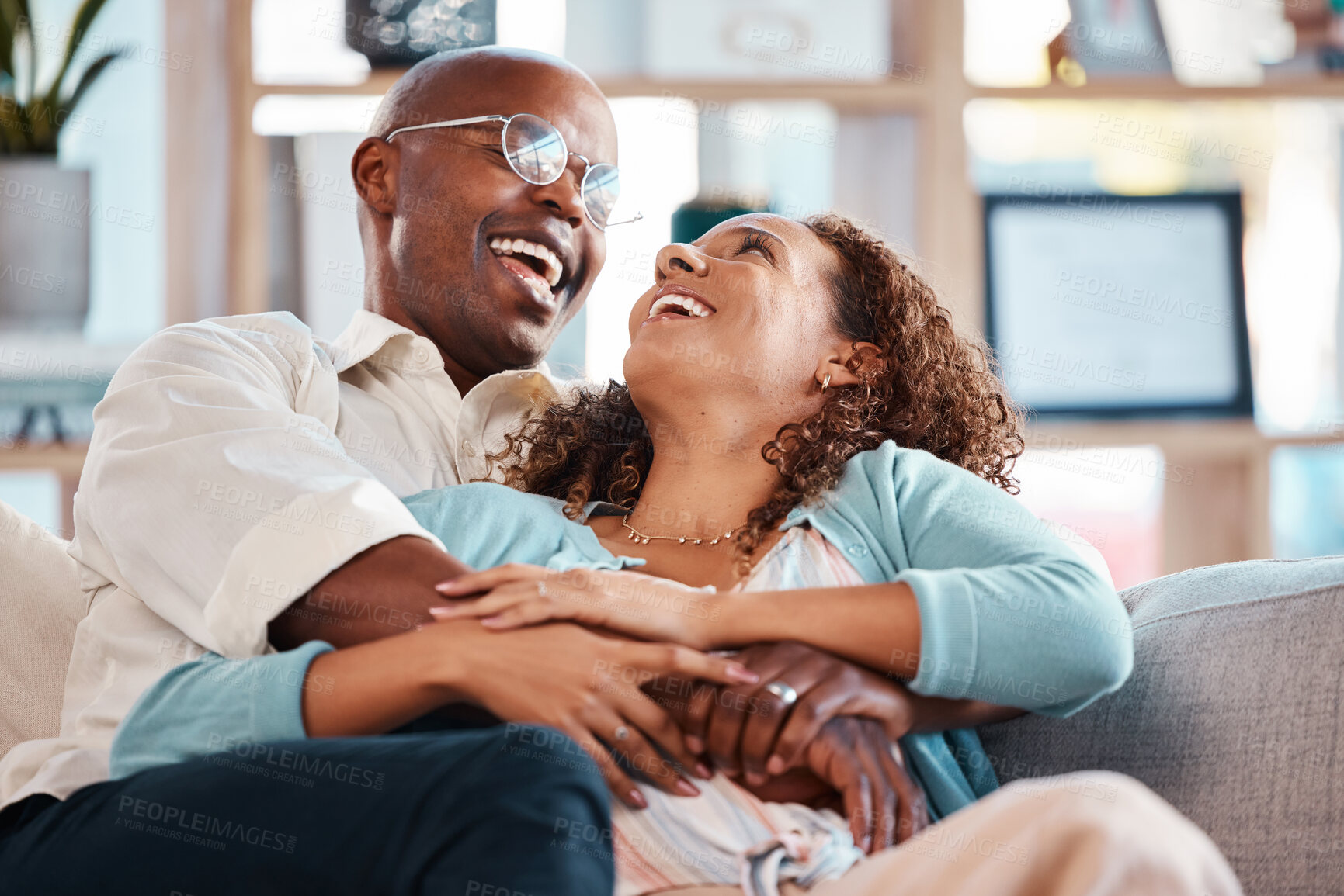 Buy stock photo Love, happy and couple laugh on sofa for bonding, quality time and relaxing together at home. Marriage, relationship and black man and woman on couch embrace, hugging and laughing for funny joke