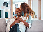 Love, happy and couple kiss on sofa for bonding, quality time and relaxing together at home. Marriage, interracial relationship and man and woman on couch embrace, hugging and laughing in living room