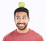 Happy, apple and balance on a head with a man in studio isolated on a white background for diet or nutrition. Smile, nutritionist and food with a healthy young male balancing fruit for detox or fiber