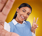 Selfie, peace sign and portrait of Indian woman in studio for happiness, confident and smile on yellow background. Emoji mockup, fashion and girl with hand gesture with beauty, cosmetics and makeup