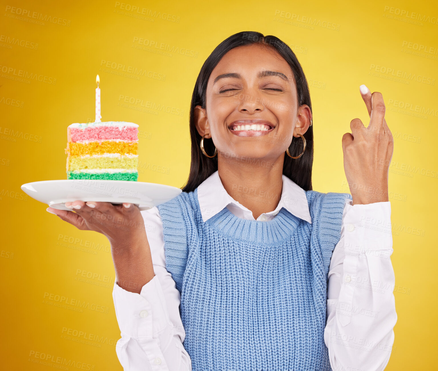 Buy stock photo Smile, wish and woman with cake in studio for happy celebration or party on yellow background. Happiness, excited gen z model with fingers crossed and candle in rainbow dessert to celebrate milestone