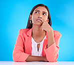 Thinking, confused and a business woman on a blue background in studio for problem solving at her desk. Idea, doubt and decision with a young female employee contemplating a thought, choice or option