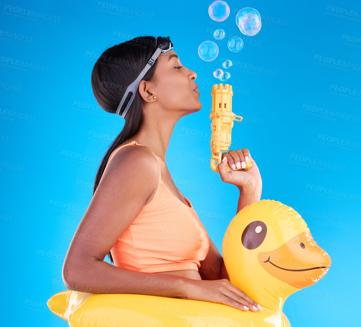 Buy stock photo Bubbles, goggles and rubber duck with a woman on a blue background in studio ready for summer swimming. Happy, travel and vacation with an attractive or playful young female blowing a bubble gun