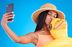 Happy woman, selfie and swimming travel for social media or profile picture with inflatable duck against a blue studio background. Excited female model in summer swimwear for photo, vacation or trip