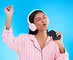 Singing, music and a woman in pyjamas with headphones isolated on a blue background in a studio. Happy, playful and a girl listening to the radio, audio or streaming songs before bedtime on a mobile