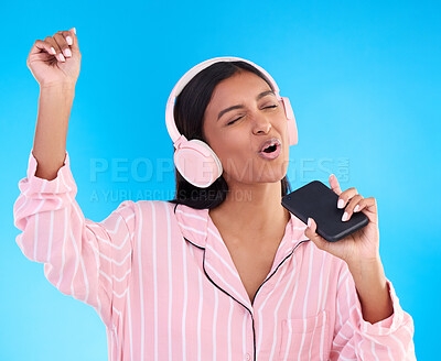Buy stock photo Singing, music and a woman in pyjamas with headphones isolated on a blue background in a studio. Happy, playful and a girl listening to the radio, audio or streaming songs before bedtime on a mobile