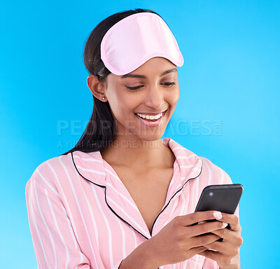 Buy stock photo Happy, bedtime and a woman typing on a phone isolated on a blue background in studio. Smile, reading and an Indian girl with social media notification, mobile chat or online communication in pyjamas
