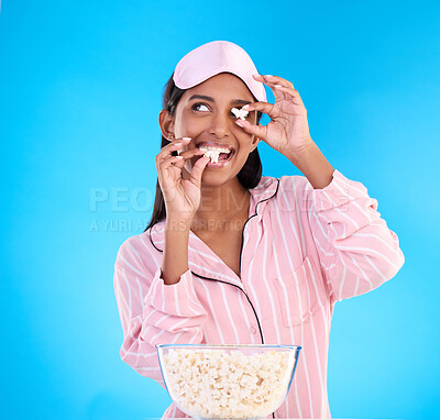 Buy stock photo Popcorn, pajamas and playful with a woman on a blue background in studio watching a movie for entertainment. Fun, video and night with an attractive young female eating a snack while streaming