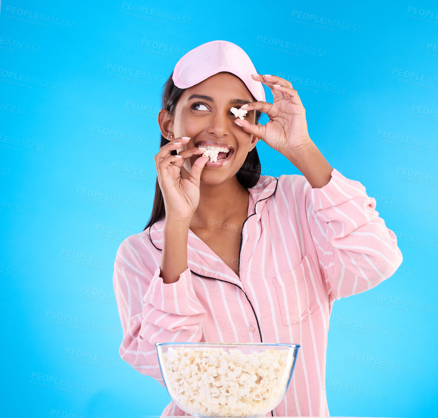 Buy stock photo Popcorn, pajamas and playful with a woman on a blue background in studio watching a movie for entertainment. Fun, video and night with an attractive young female eating a snack while streaming