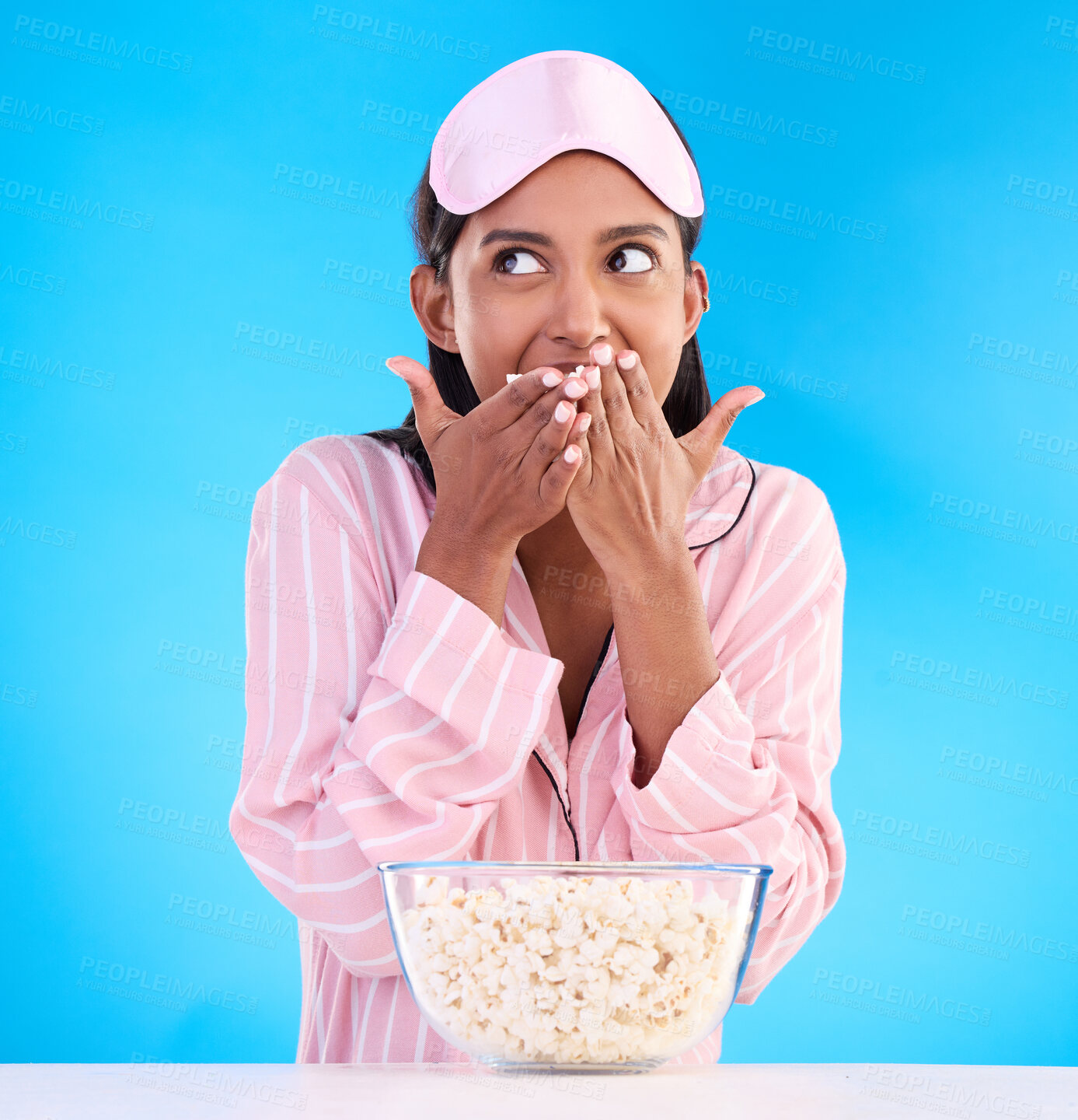 Buy stock photo Popcorn, pajamas and thinking with a woman on a blue background in studio watching a movie for entertainment. Idea, video and night with an attractive young female eating a snack while streaming