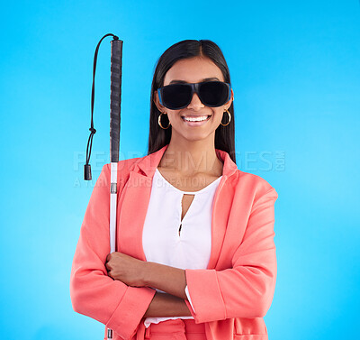 Buy stock photo Blind, disability and sunglasses with a woman on a blue background in studio holding her walking stick. Portrait, vision and smile with an attractive young female arms crossed for disabled lifestyle