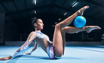 Woman, gymnastics and ball between legs of performance, competition training or dancing in dark sports arena. Female athlete, rhythmic movement and creative talent in solo concert, agility or balance