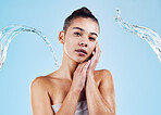 Water splash, portrait and woman shower in studio, blue background and healthy beauty of natural skincare. Serious female model, wet and cleaning for hygiene, hydration and wellness on color backdrop
