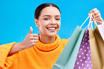 Buy stock photo Happy woman, face and shopping bags with thumbs up for purchase, sale or discount against a blue studio background. Portrait of female shopper holding gift bag showing thumb emoji, yes sign or like