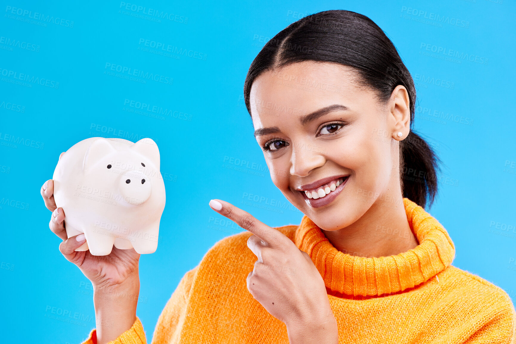 Buy stock photo Happy woman, money and pointing to piggy bank for investment, budget or finance against blue studio background. Portrait of female with savings, cash or coin for profit investing or financial freedom