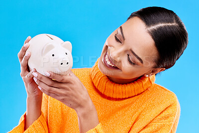 Buy stock photo Happy woman, money and piggy bank for investment, budget or finance against a blue studio background. Female smile holding savings of cash or coin for change, profit or investing in financial freedom