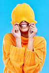 Fashion, crazy and cover with woman and beanie in studio for hiding, winter and goofy. Playful, happiness and smile with female and knitted hat isolated on blue background for funny, silly and cool