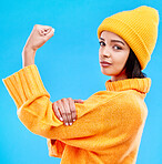 Portrait of woman in winter fashion with power, beanie and glasses isolated on blue background. Style, arm flex and gen z girl in studio backdrop with strong face and warm clothing for cold weather.