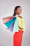 Portrait, shopping and sales with a woman customer in studio on a gray background for retail or consumerism.  Fashion, luxury or smile with an attractive young female carrying bags over her shoulder