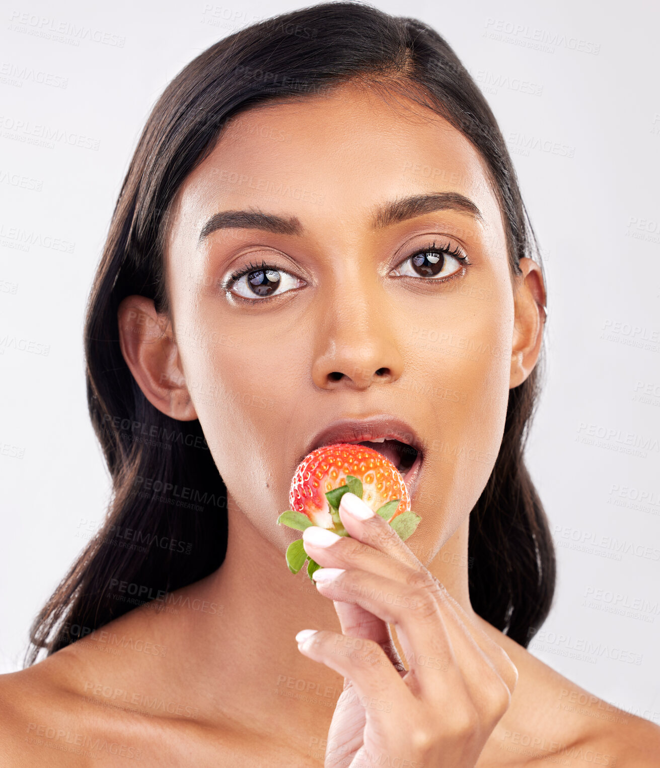 Buy stock photo Portrait, beauty and a woman biting a strawberry in studio on a gray background for health, diet or nutrition. Face, skincare and serious with an attractive young female model eating a fruit berry