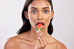 Portrait, skincare and a woman biting a strawberry in studio on a gray background for health, diet or nutrition. Face, beauty and serious with an attractive young female model eating a fruit berry