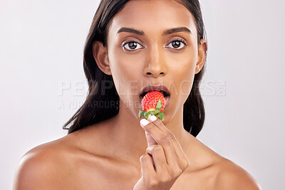 Buy stock photo Portrait, skincare and a woman biting a strawberry in studio on a gray background for health, diet or nutrition. Face, beauty and serious with an attractive young female model eating a fruit berry
