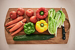 Vegetables, cutting board and healthy food on the counter in the kitchen for a vegan meal. Crops, wood and diet with fresh, organic and natural produce with a knife for cooking a vegetarian dinner.