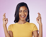 Fingers crossed, wish and woman in a studio with hope, prayer or faith for success or achievement. Happy, smile and Indian female model with a luck hand gesture or sign isolated by purple background.