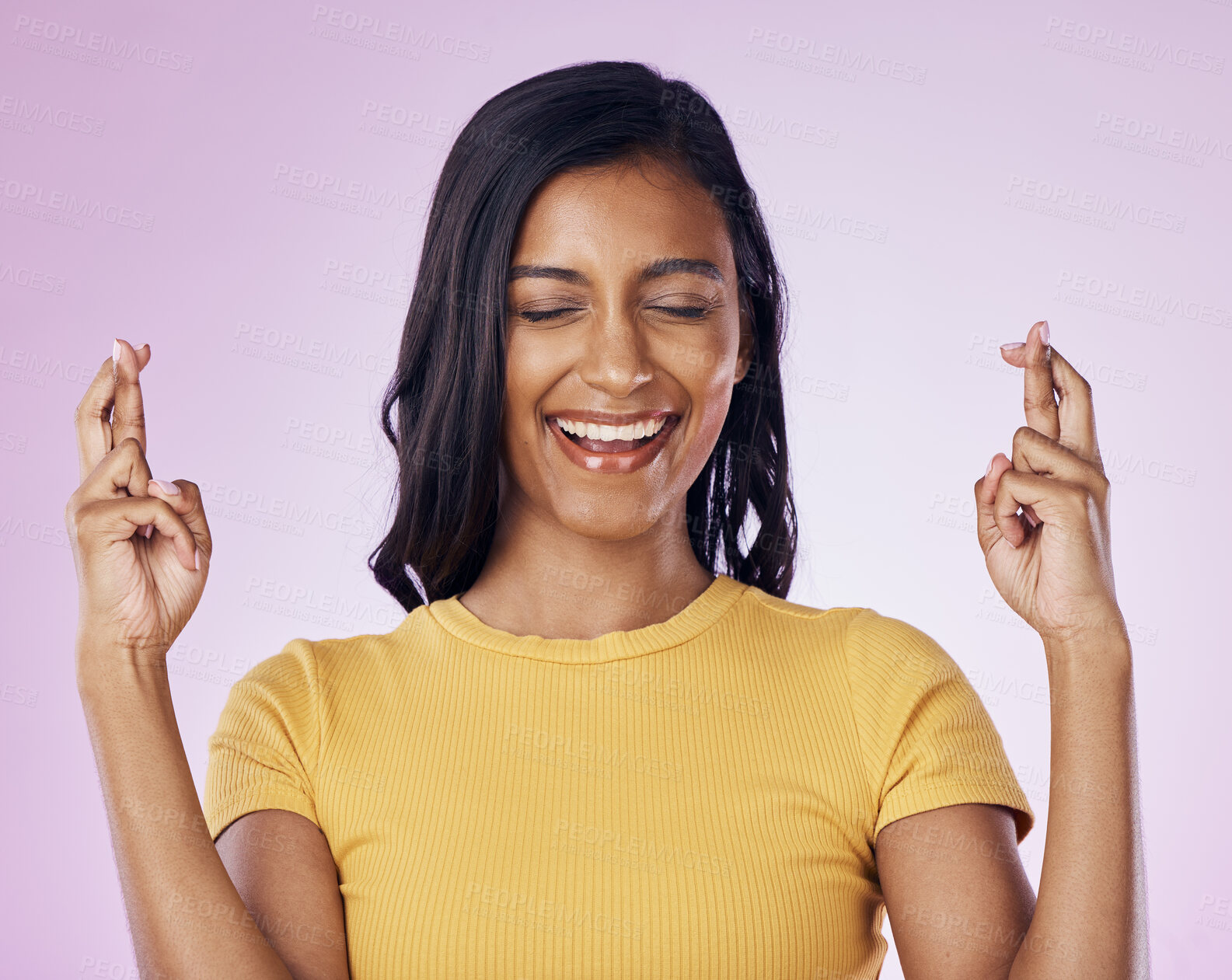 Buy stock photo Fingers crossed, wish and woman in a studio with hope, prayer or faith for success or achievement. Happy, smile and Indian female model with a luck hand gesture or sign isolated by purple background.