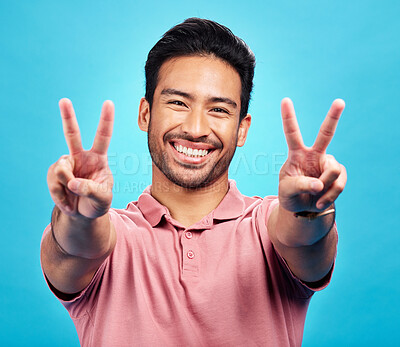 Buy stock photo Portrait, peace sign and Asian man with a smile, support and confident on a blue studio background. Face, male person or model with v gesture, emoji and symbol with happiness, hands and peaceful icon