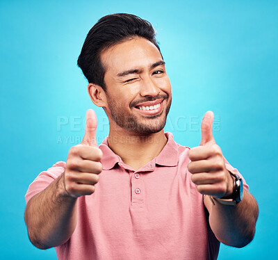Buy stock photo Portrait, thumbs up or wink by man in studio in positive, feedback or review on blue background. Face, smile and hand gesture by Asian male model showing yes, agreement or vote emoji while isolated