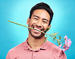 Teeth, flower and happy with portrait of man in studio for celebration, gift and romance. Funny, goofy and present with male isolated on blue background for happiness, smile and valentines day mockup