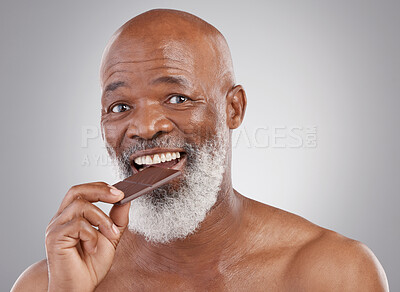 Buy stock photo Black man, portrait and eating chocolate sweets isolated on a studio background for a treat. Happy, snack smile and an elderly African model biting into a sweet candy bar for happiness and sugar