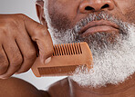 Senior black man, hands and beard with comb in grooming, beauty or skincare hygiene against a studio background. Closeup of African elderly male face combing or brushing facial hair in clean wellness