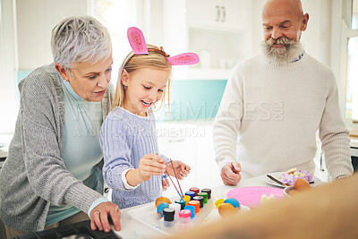 Buy stock photo Easter, art and a girl painting with her grandparents in their home for love, bonding or celebration together. Family, kitchen or egg with a senior couple and their grandchild in a house to paint