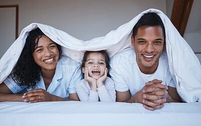 Buy stock photo Happy, love and portrait of a family on a bed in their bedroom relaxing and bonding together. Happiness, smile and girl child laying with her mother and father with a blanket in their modern home.