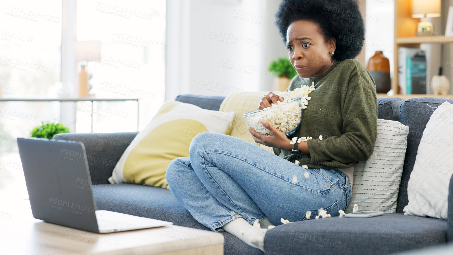 Buy stock photo African woman, watching and horror movie on a laptop eating popcorn on a living room couch. Scared female person, home lounge and online series with film snack and food with scary video on computer